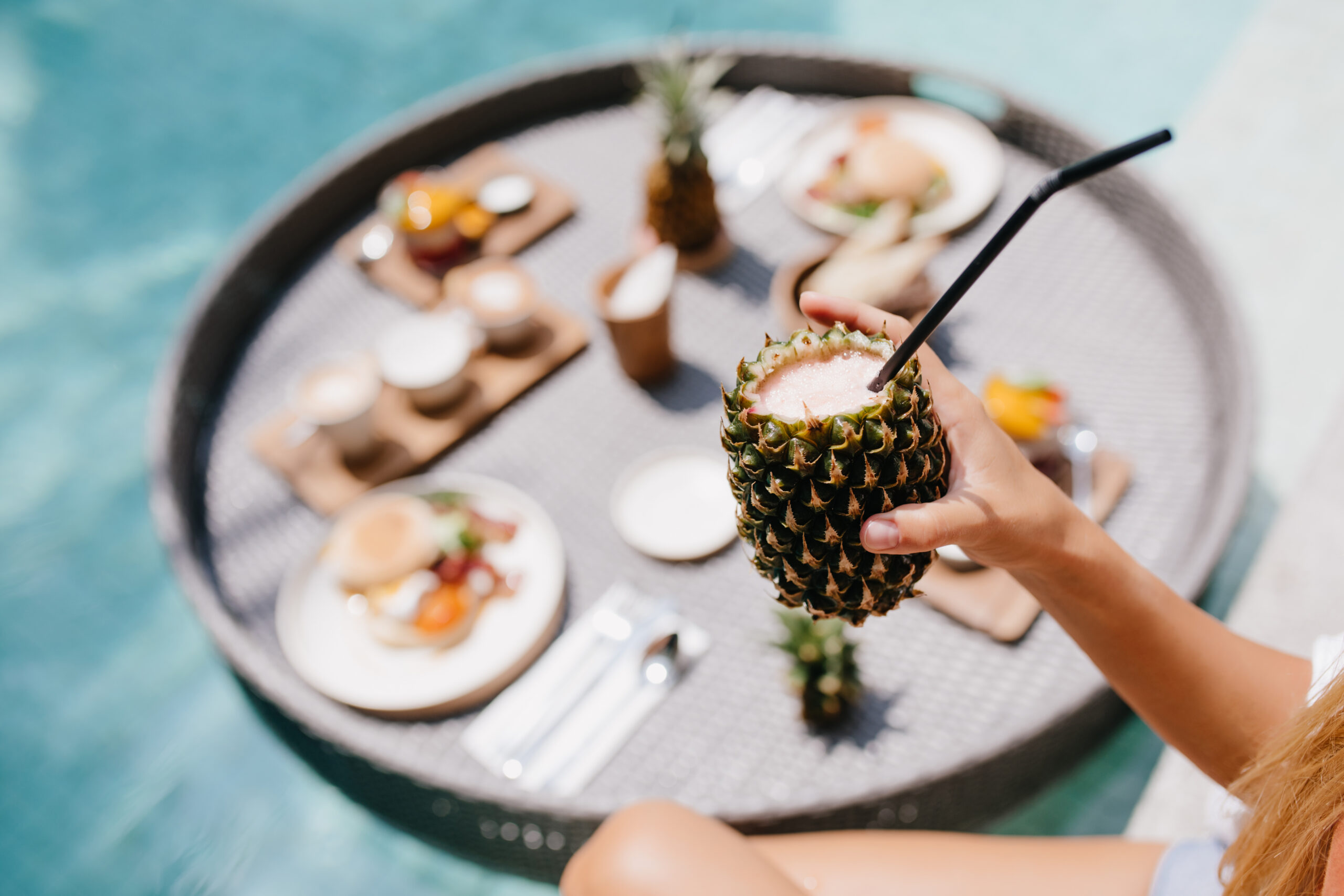 Tanned woman holding sweet pineapple cocktail. Female model posing during lunch in pool.